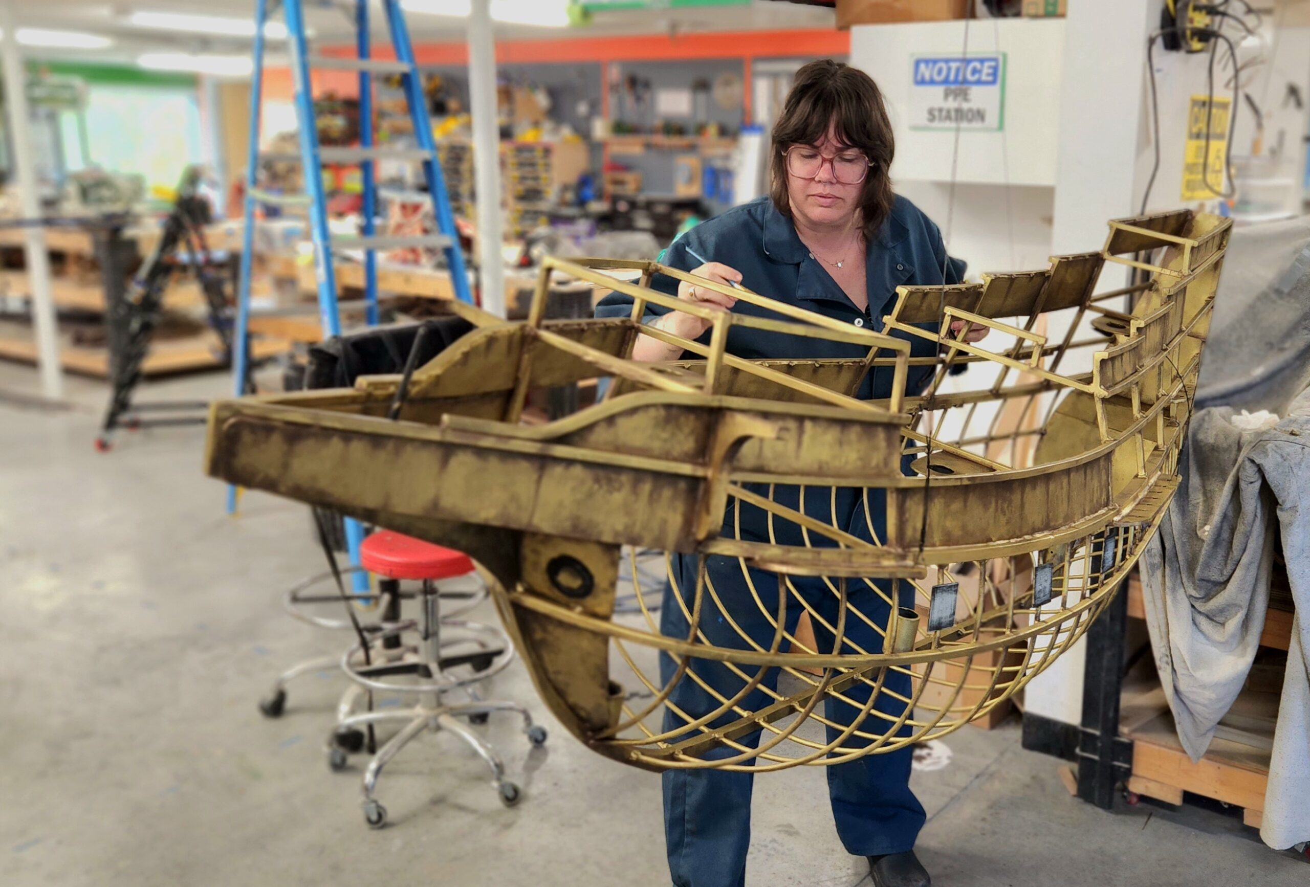 woman working on the back side of a suspended metal sculpture of the hull of a ship